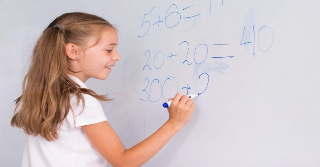 A girl engages with a whiteboard for factors and multiples practice.