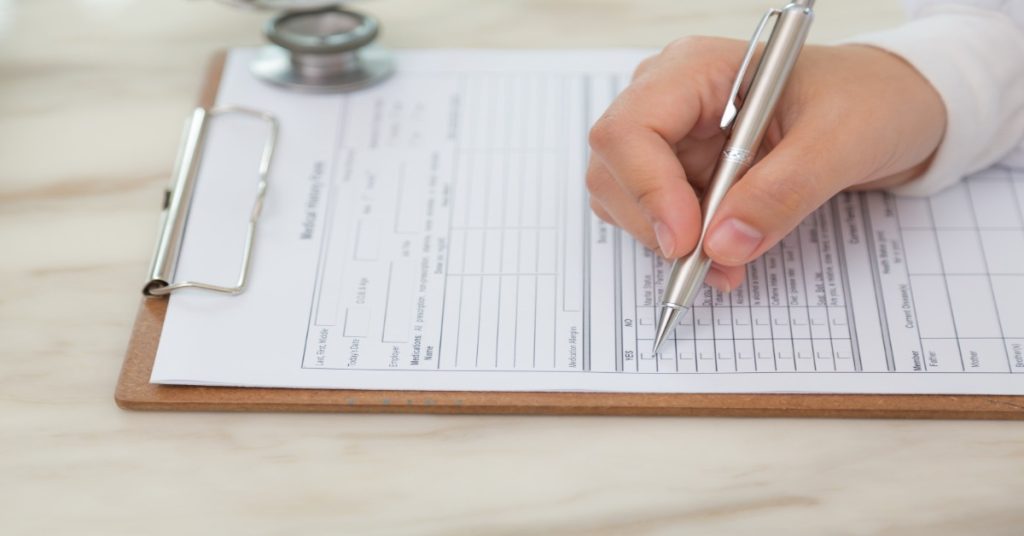 A person writes on a clipboard with a pen, completing the dance class admission form for 2025.