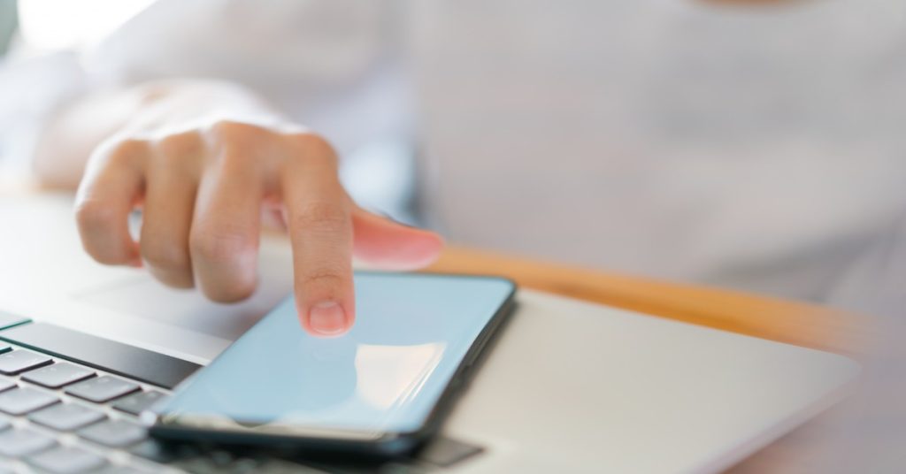 Person using a smartphone while working on a laptop, analyzing metrics for user engagement, focusing on CTR.
