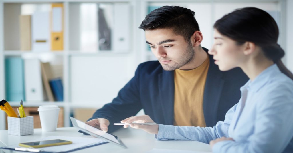 A man and woman are seated at a table with a tablet, focusing on open-ended questions and understanding their answers.