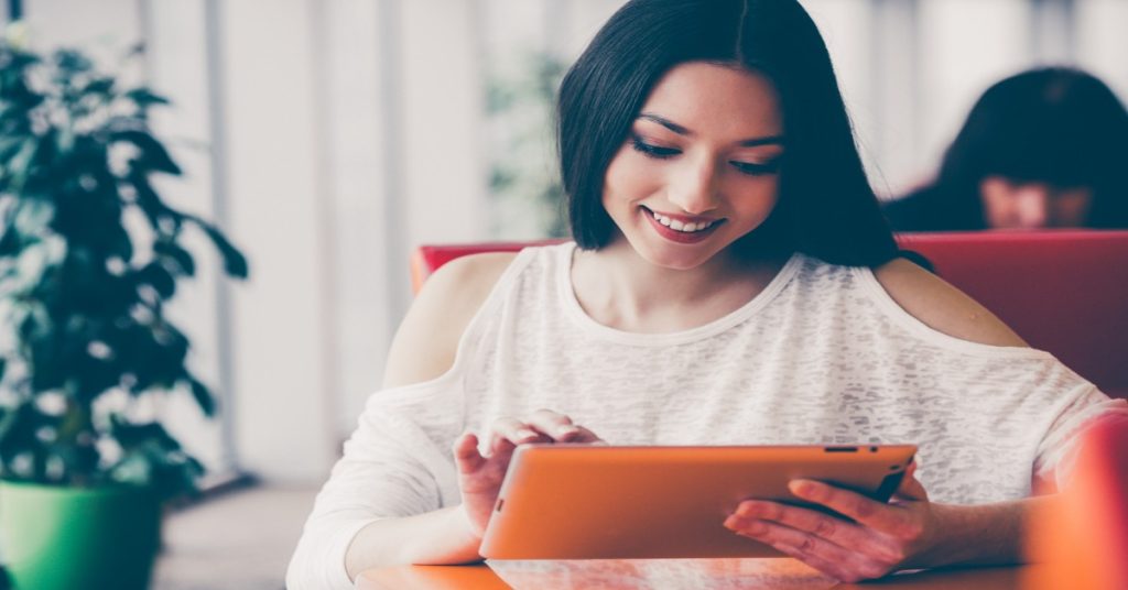 A woman sitting at a table with her tablet, filling an online survey. 