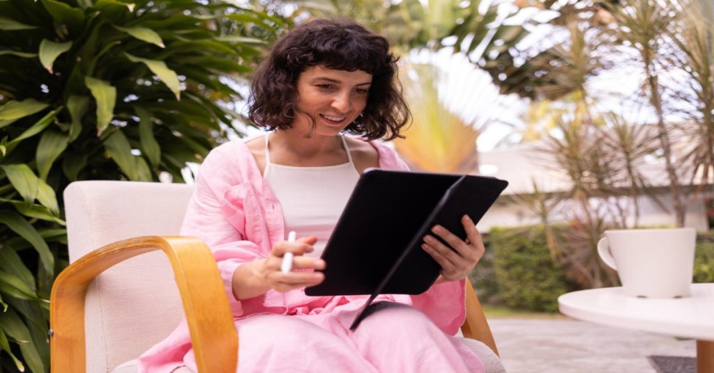 A woman in a pink robe sits on a chair, using tablet for reading reviews manually for sentiment classification.